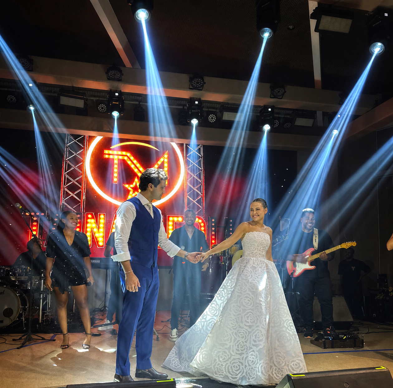 Tainá canta enquanto os noivos dançam de mãos dadas diante da banda e os músicos celebram sorrindo