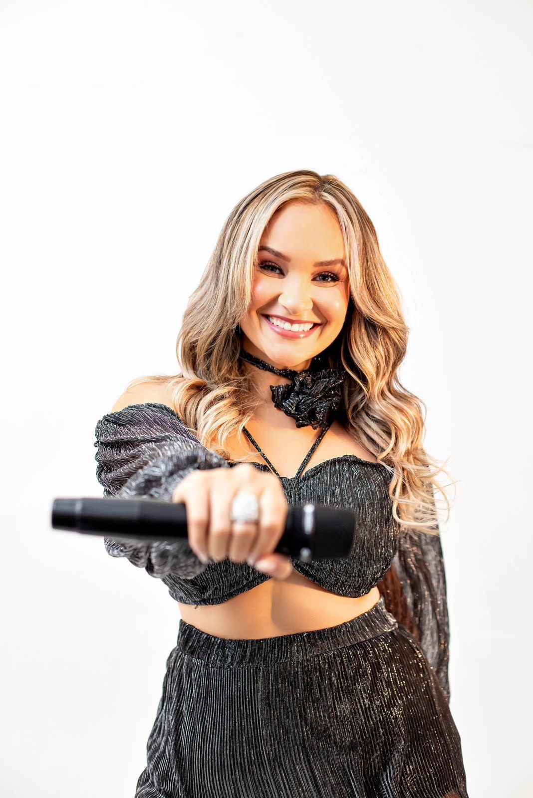 Tainá Meoli apontando o microfone para a câmera, sorrindo