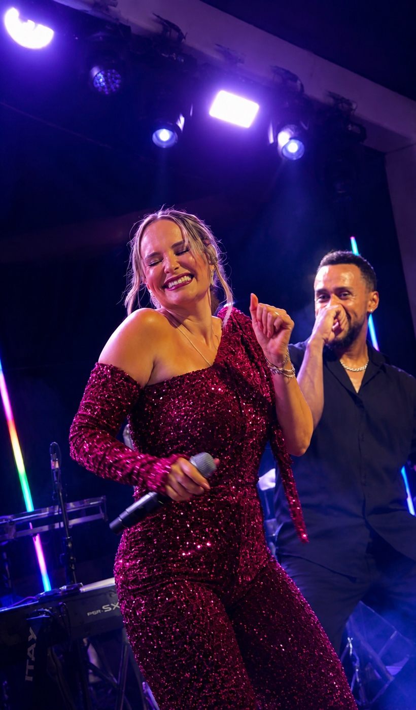 Tainá Meoli sorrindo e dançando com microfone no palco